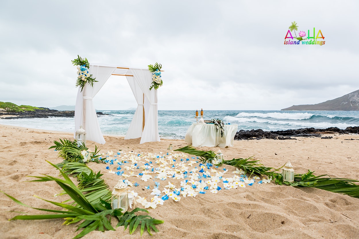 White wedding arch with light blue flowers, candles and palm fronds on the sand